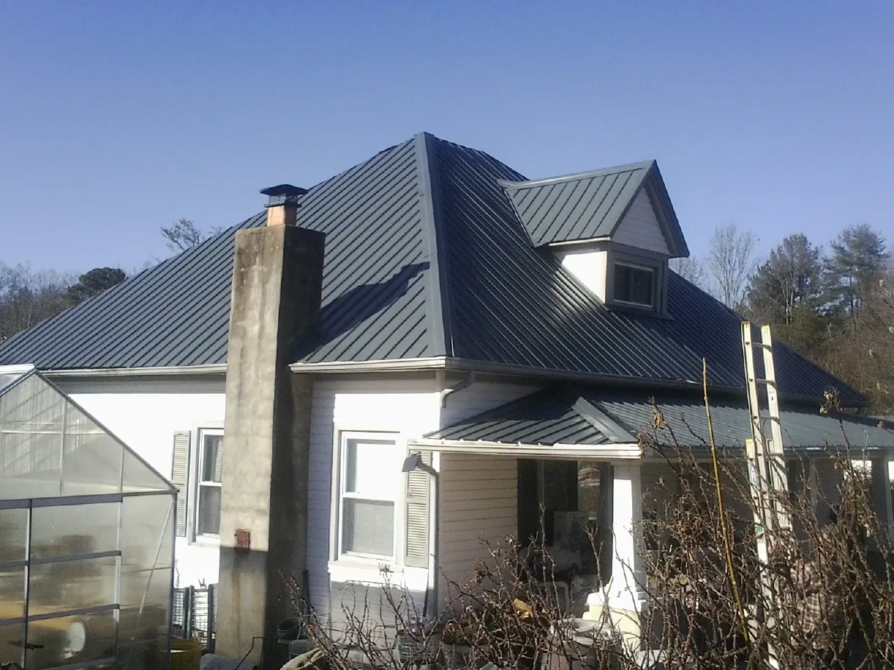 Dark blue standing seam metal roof on a white farmhouse with dormer — Slate & Tile Roof Repair by Roofing Brothers in Prides Crossing