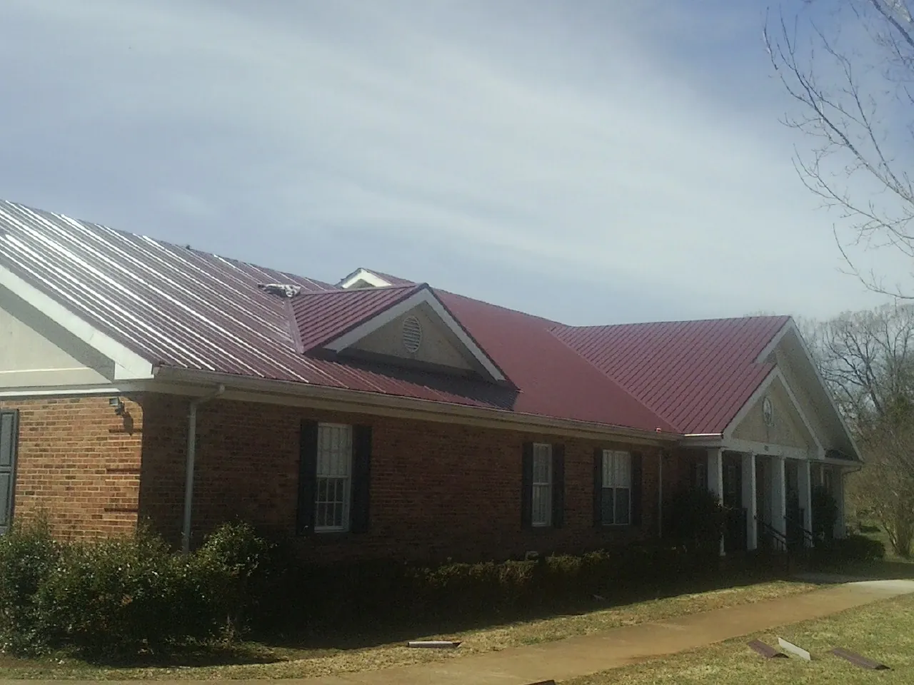 Red metal roof with gabled entries on a long brick building, from a Hail Damage Roof Repair job in Prides Crossing