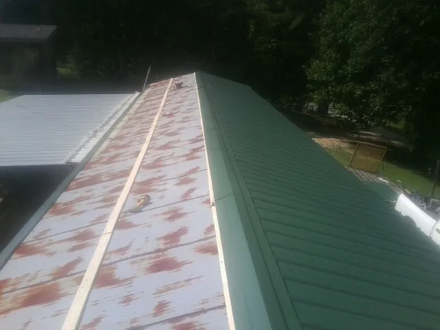 Old rusted panels beside newly installed green metal roofing — Wind Damage Roof Repair by Roofing Brothers in Prides Crossing