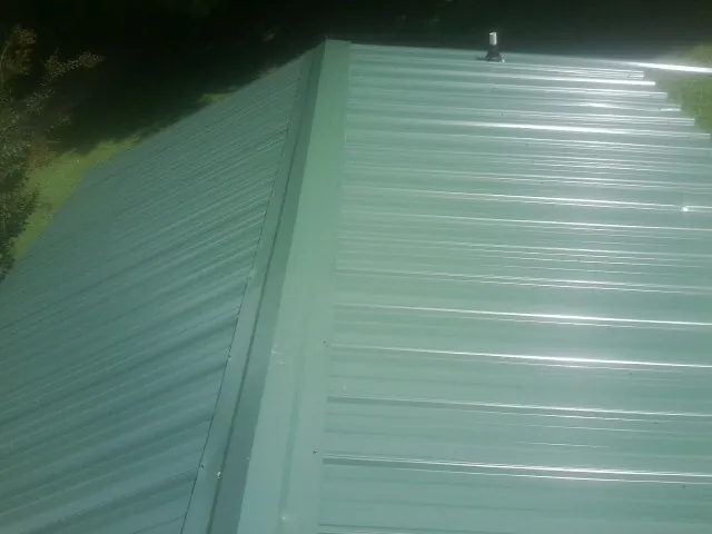 New green metal panels meeting at the ridge of a roof — Flat Roof Repair work by our crew in Prides Crossing