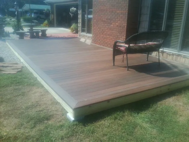 New wood deck and wicker chair beside a brick house in Prides Crossing