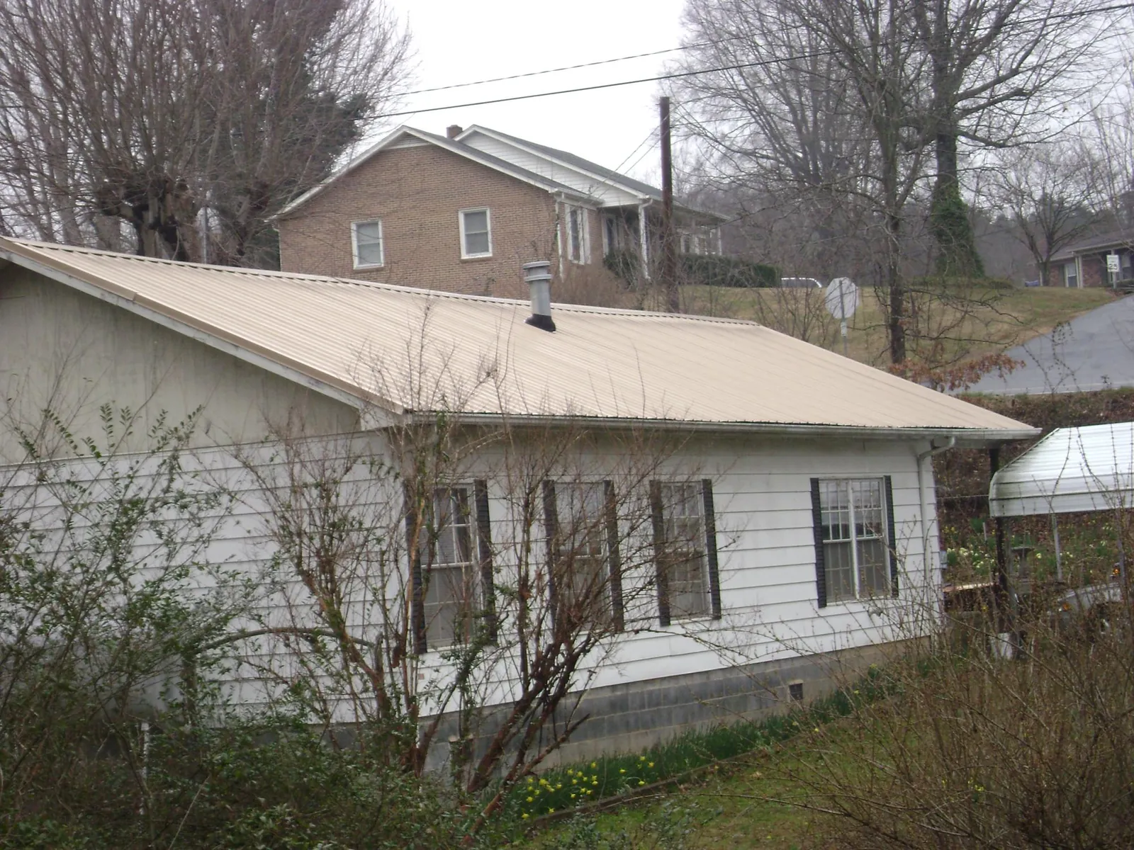 Tan metal roof on a white sided house set into a hillside — Commercial Roofing by Roofing Brothers in Prides Crossing
