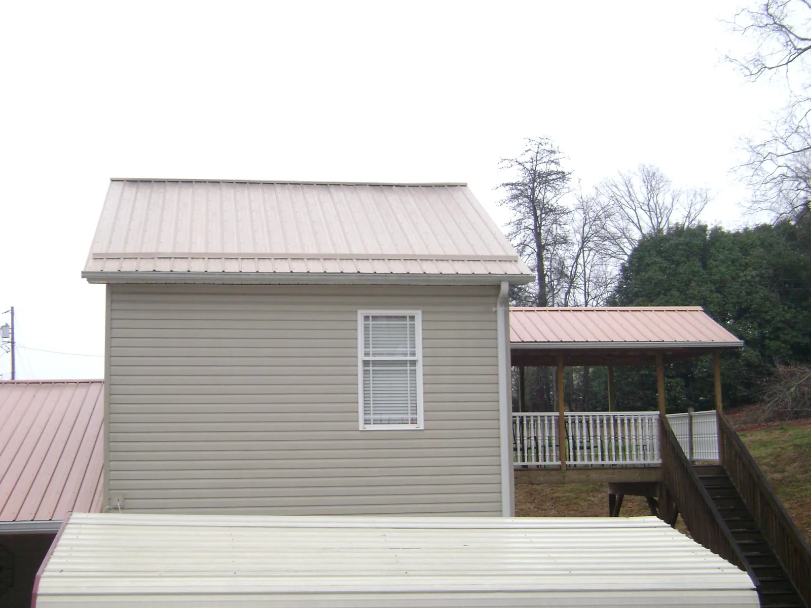 Tan metal roofs on a two story addition and attached porch, from a Roof Replacement job in Prides Crossing